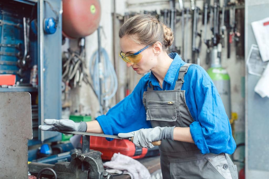 Woman worker in metal workshop deburring workpiece — Photo