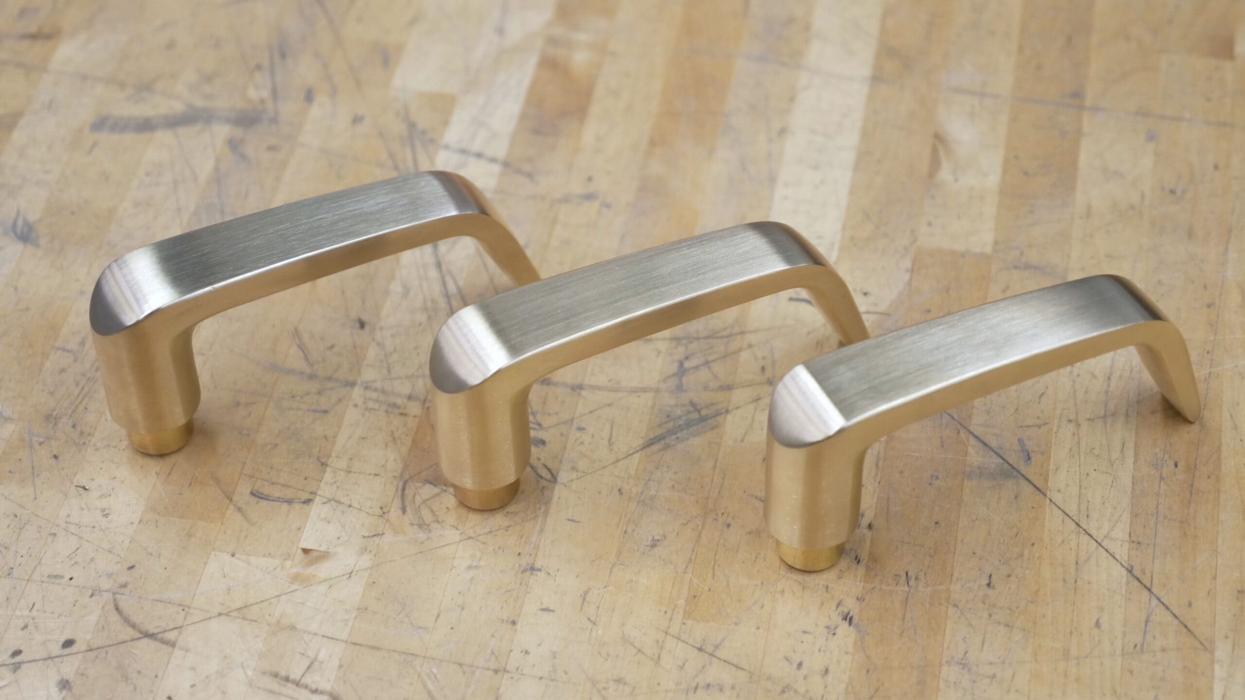 Three-Brass-Door-Handles-on-a-Wooden-Table-scaled